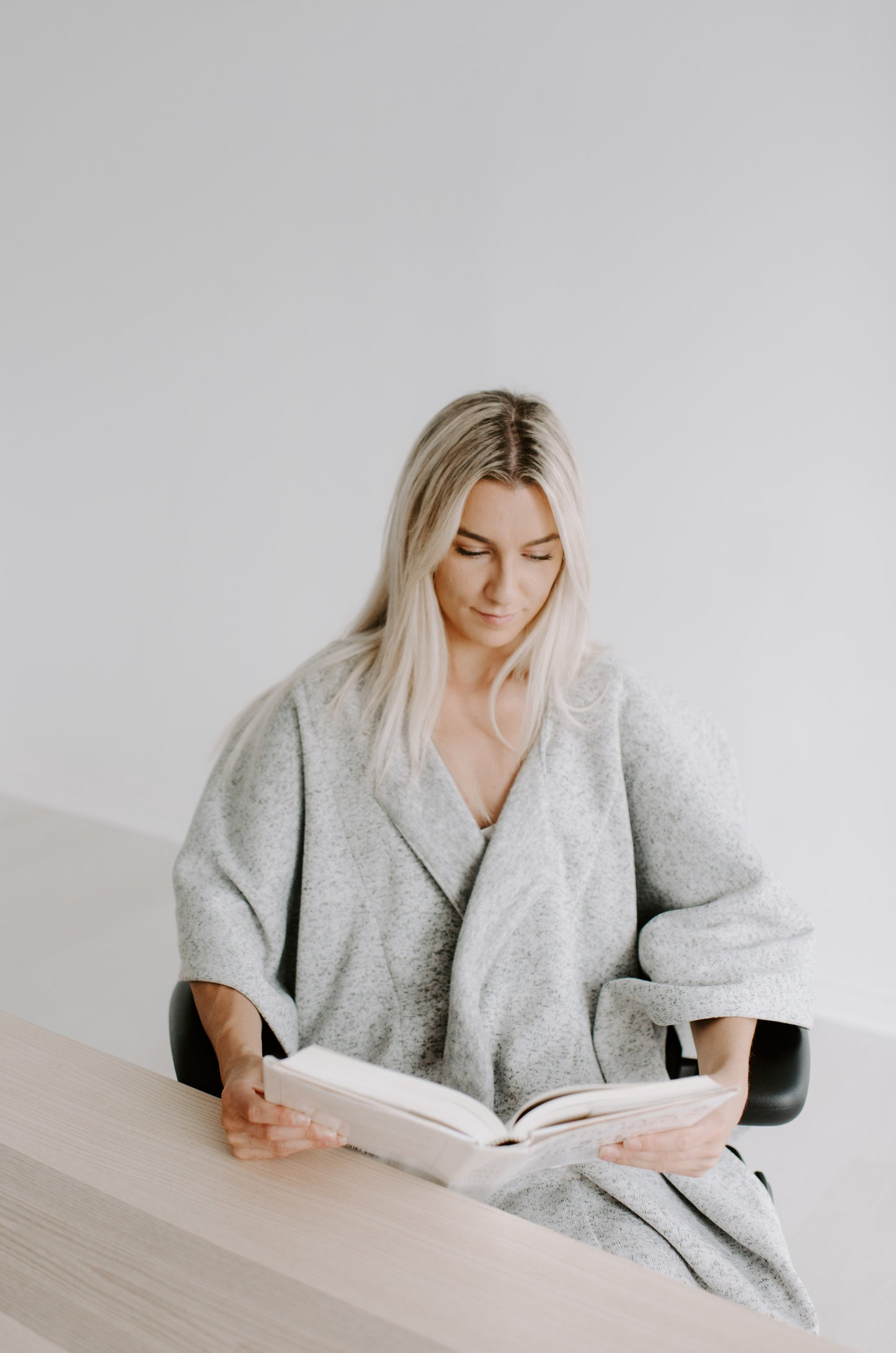 Woman sitting comfortably, reading while wrapped in a Warmür office chair blanket at her workspace