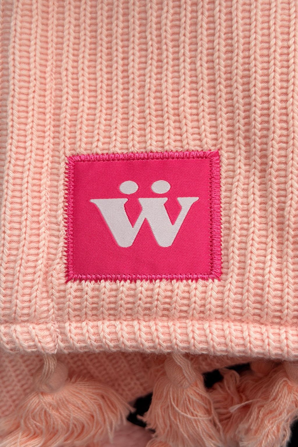 A pink tag with a warmur logo on the pink office chair blanket