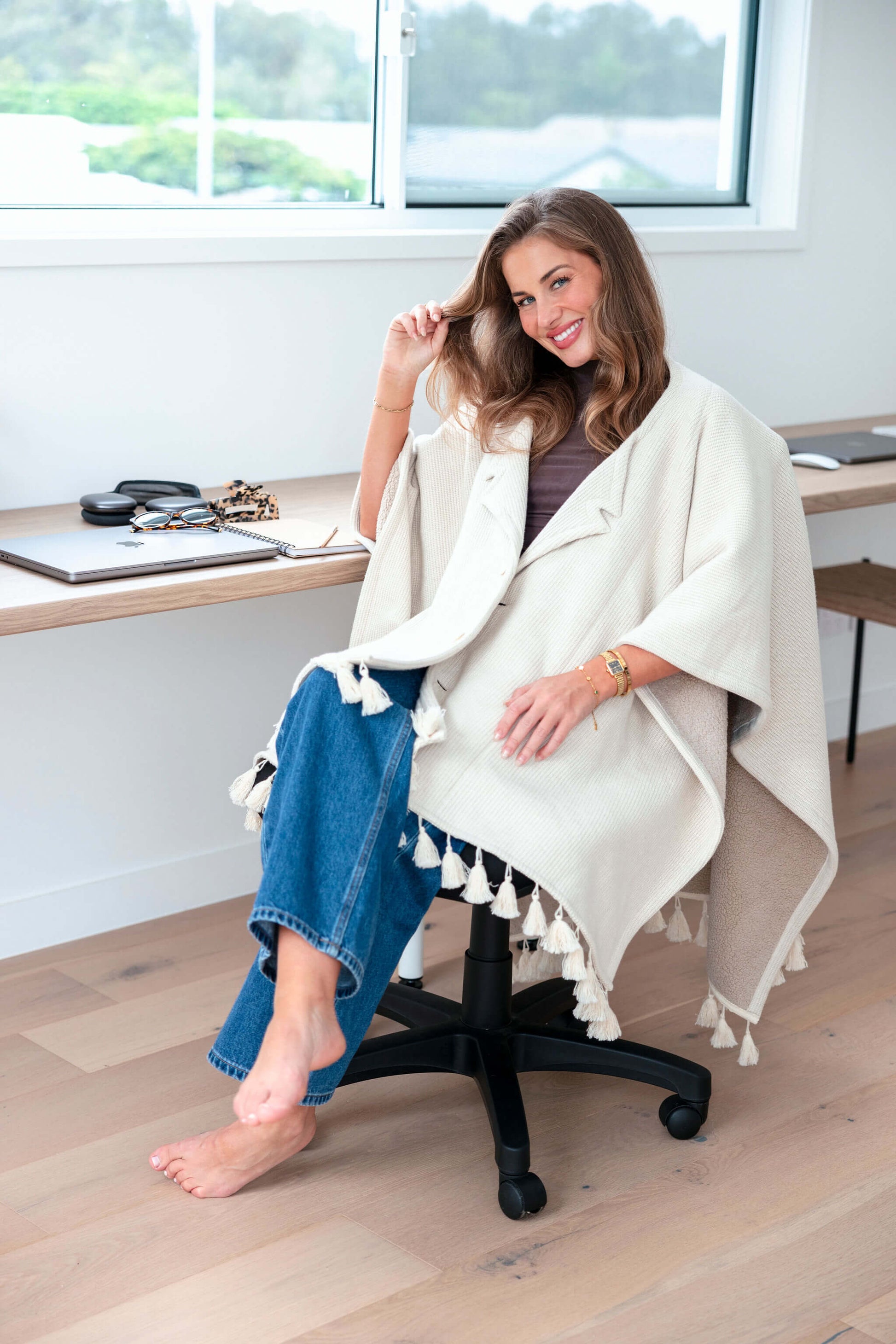 Woman working at her desk wrapped in a beige office chair blanket that stays in place while she types on her laptop.