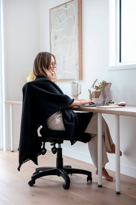 Professional woman in a modern office wearing the black Warmür office chair blanket, staying warm during meetings while maintaining a sleek and polished look.