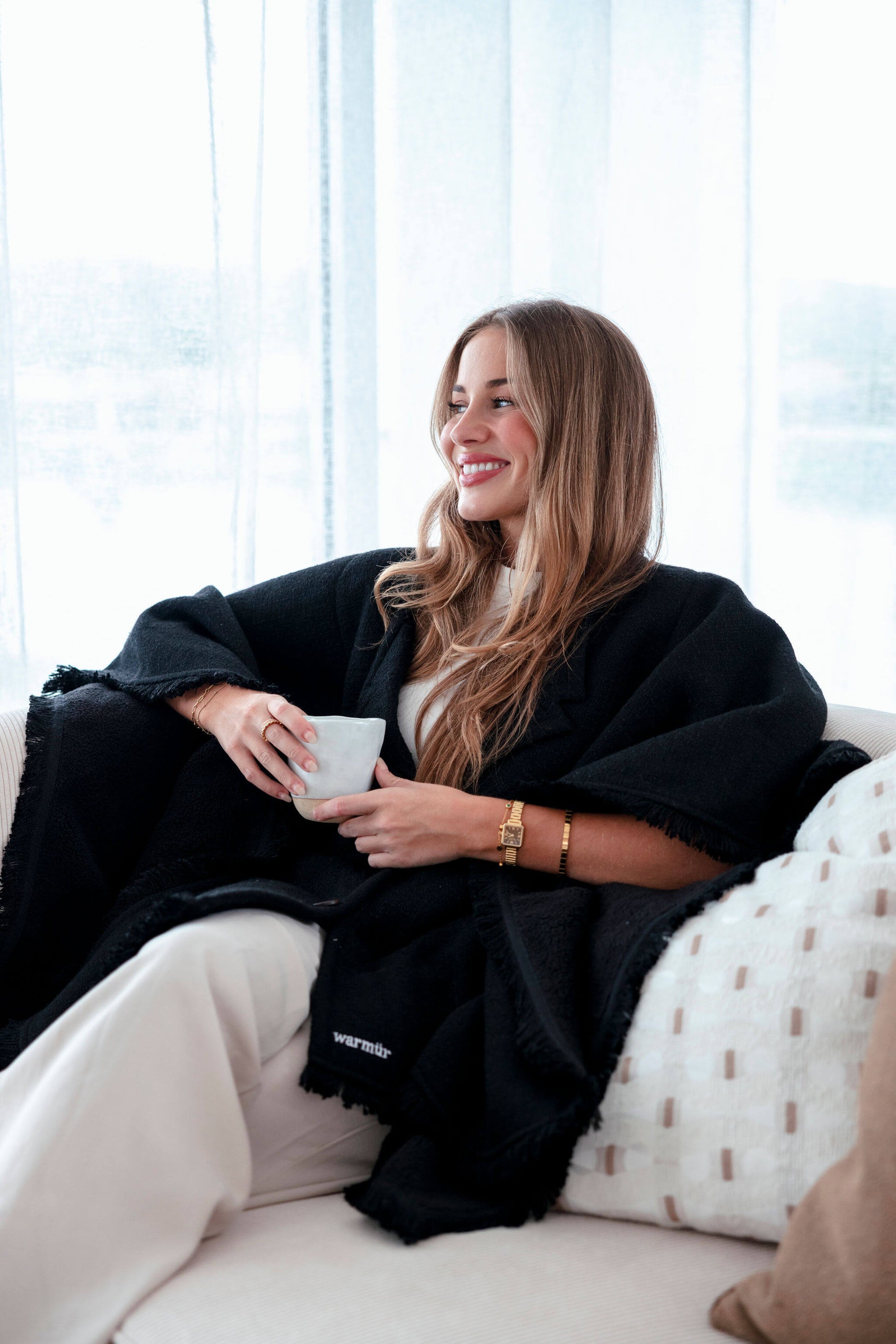 Business professional sitting at her workstation with the black Warmür, a premium office chair blanket that complements a modern minimalist workspace.