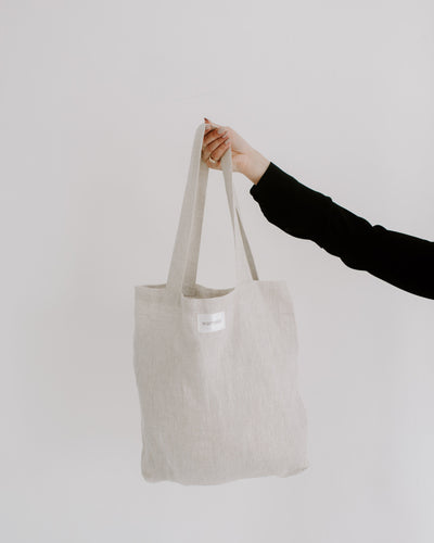 A beige linen tote bag with long straps, held up against a white background, perfect for the market. 